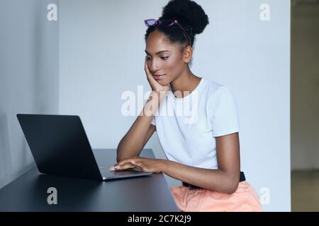 Young beautiful casual African American woman dreamily working on laptop in office Stock Photo
