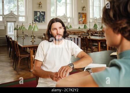 Young thoughtful student taking verbal exam to teacher in lecture room of university Stock Photo