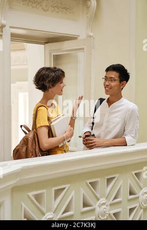 Two young smiling international students happily talking at break in corridor of university Stock Photo
