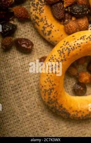 Small bagels and dried rosehip fruit scattered on a homespun cloth with a rough texture. Close up Stock Photo
