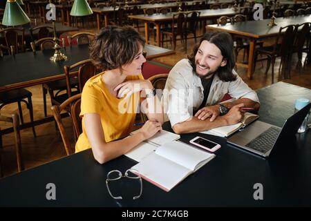 Two young students happily studying together with laptop and books in library of university Stock Photo