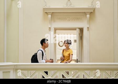 Two young attractive casual international students thoughtfully talking at break in corridor of university Stock Photo
