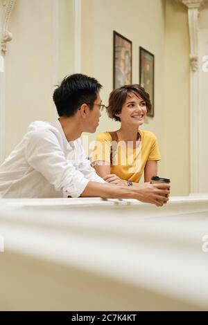 Two young attractive international students happily talking at break in corridor of university Stock Photo