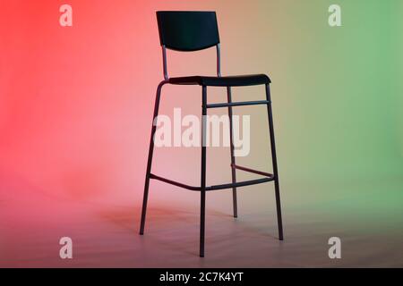A tall chair stands in a photo studio on a white paper background lit in red-green tones Stock Photo