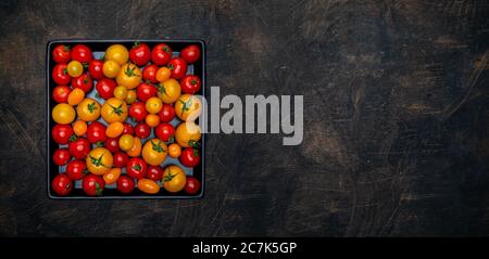 Pile of fresh red and yellow cherry tomatoes in black ceramic tray on vintage table. Overhead shot with copy space. Stock Photo