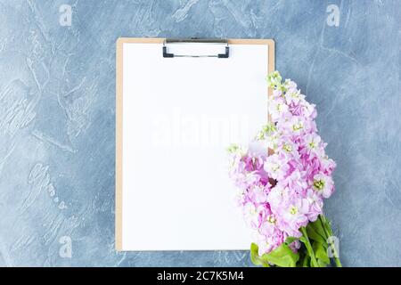 Clipboard with white blank paper and flowers on white background. Concept Female workspace Mockup Top view Flat Lay. Space for text.