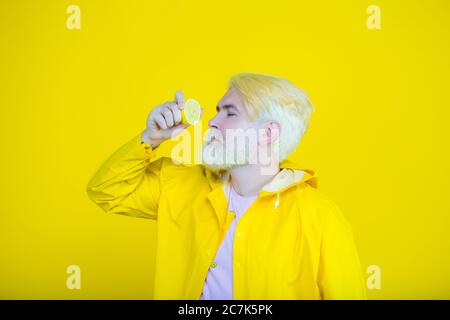 Happy bearded hipster man eating sliced lemon over yellow background. Man with long beard hold lemon. Citrus vitamin. Stock Photo
