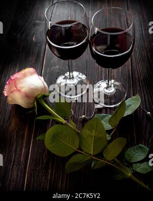 Two glasses of red wine and a rose located on a vintage wooden table Stock Photo
