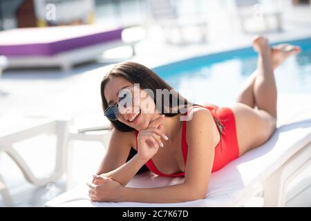 Beautiful brunette in red swimming suit lying on the chaise lounge and smiling Stock Photo