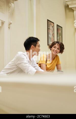 Two young attractive casual international students joyfully talking at break in corridor of university Stock Photo