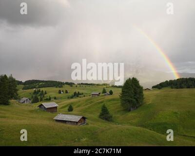 Gentle hilly landscape with huts, rainbows and mountains in the rain, storm on the Alpe di Siusi Stock Photo
