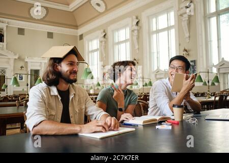 Group of young joyful multinational students happily fooling around while studying together in library of university Stock Photo