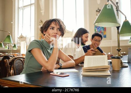 Beautiful female student sitting with book while dreaming during lecture in university Stock Photo