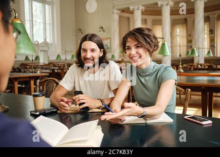 Young smiling casual students joyfully discussing project together in library of university Stock Photo