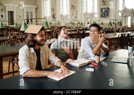 Group of young happy multinational students joyfully fooling around while studying together in library of university Stock Photo