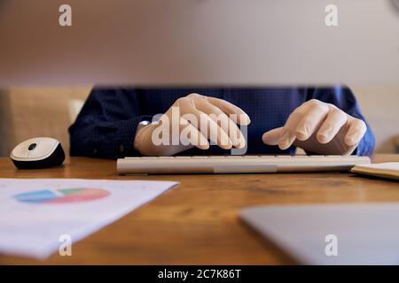 Anonymous Businessman working at desk wearing protective gloves typing on keyboard. Stock Photo