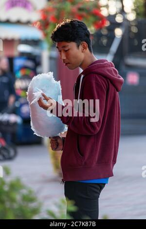 Young man in a hoodie eating blue cotton candy Stock Photo