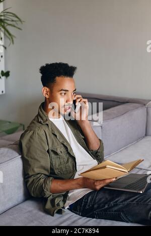 Young attractive African American man with notebook confidently talking on cellphone in co-working space Stock Photo