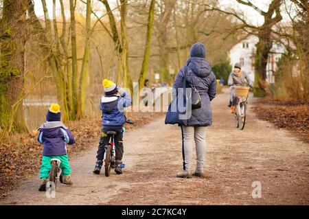 POZNAN, POLAND - Jan 12, 2020: Woman and two small kids on bicycles on a footpath in the Debiec park on a cold winter day. Stock Photo