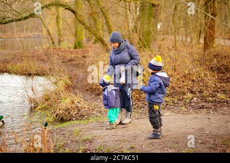 POZNAN, POLAND - Jan 12, 2020: Woman and two kids standing by a pond feeding ducks in the Debiec forest. Stock Photo