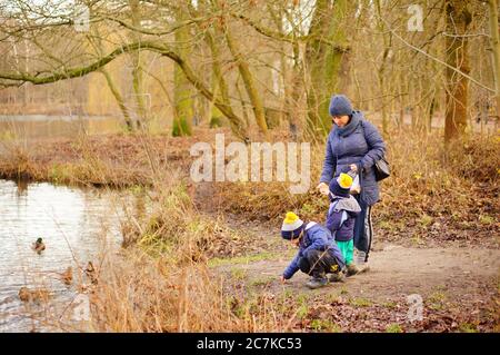 POZNAN, POLAND - Jan 12, 2020: Woman and two kids standing by a pond feeding ducks in the Debiec forest. Stock Photo