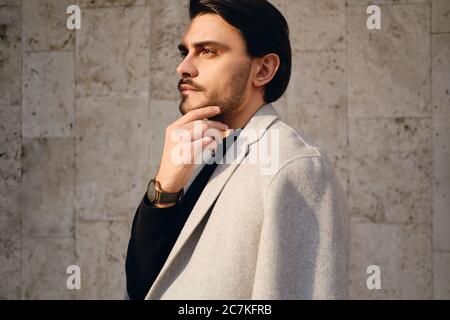 Side view of young handsome man in coat thoughtfully looking away outdoor Stock Photo