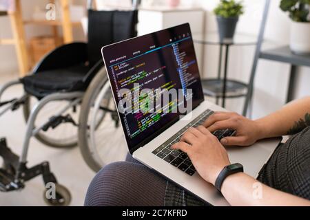 Hands of young contemporary disable female programmer touching keys of laptop keypad while sitting and working in home environment Stock Photo