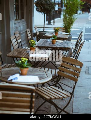 Outdoor cafe with wooden chairs and tables surrounded by buildings under the sunlight
