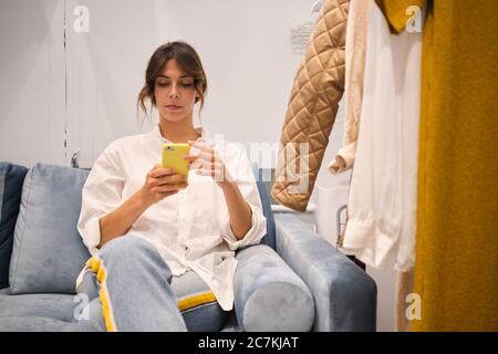 Young stylish fashion consultant confidently working on cellphone on sofa in showroom Stock Photo