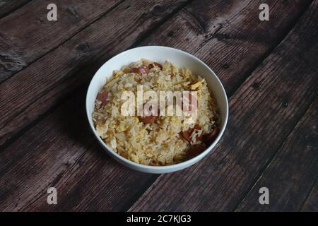 Aerial shot of fried rice with egg and sliced sausages in a bowl on a wooden table Stock Photo