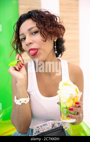 Portrait of a Latin American woman happily tasting an ice cream. Selective focus. Summer and lifestyle concept. Stock Photo