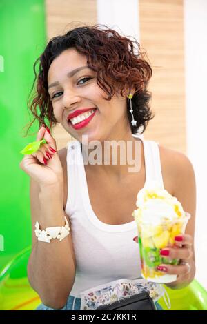 Portrait of a brown-skinned woman smiling while holding an ice cream in her hands. Selective focus. Summer and lifestyle concept. Stock Photo