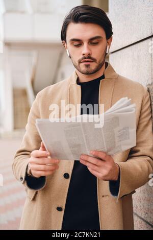 Young attractive man in beige coat reading newspaper outdoor Stock Photo