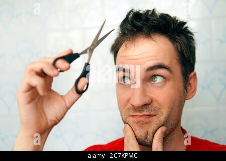 Young Man cutting his Own Hair using Scissors during Quarantine from Covid 19 - Coronavirus. fear of cutting hair. Clean yourself up on your own. Stock Photo