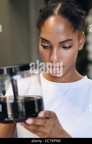 Portrait of serious African American girl thoughtfully holding coffee pot in modern office Stock Photo
