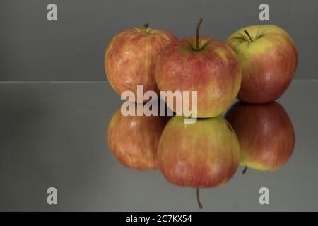 Three red apples on mirroring table on mirror gray background with reflection isolated close up Stock Photo