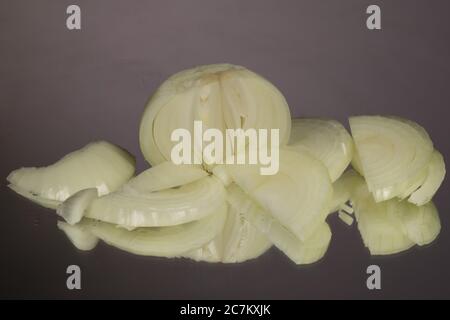 Pile of whole and cut onions with. On a gray glossy background with reflection. Stock Photo