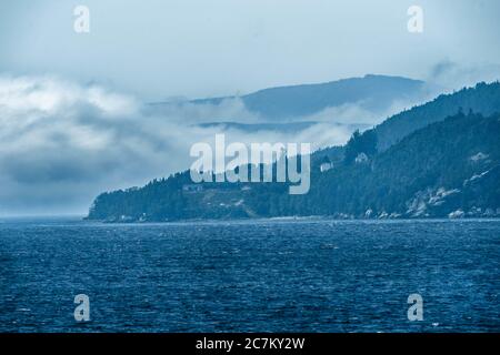Breathtaking shot of a deep blue ocean and a mountain range and thick fog on a stormy day Stock Photo
