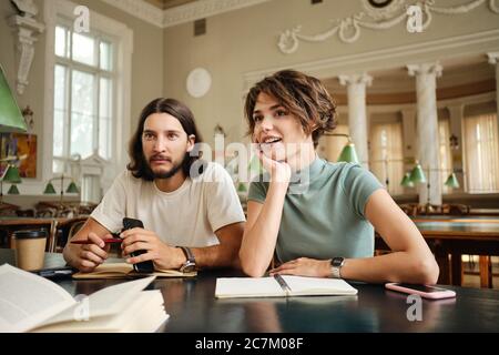 Young attractive casual students with book discussing project while studying together in library of university Stock Photo