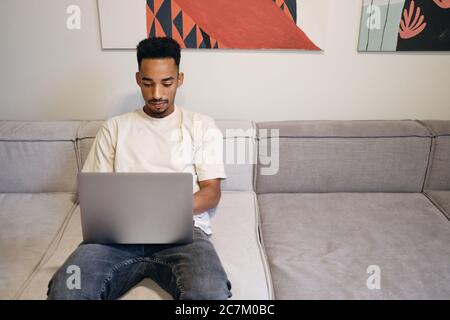 Young handsome African American guy thoughtfully working on laptop on sofa in co-working space Stock Photo
