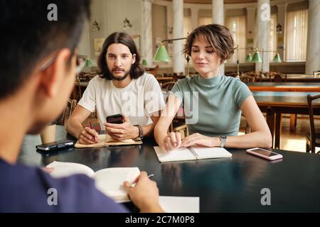 Young attarctive casual students doing homework together in library of university Stock Photo