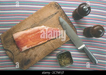 High angle shot of raw salmon on a chopping board with a knife and different seasonings Stock Photo