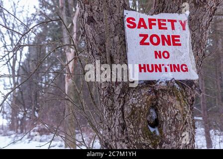 Selective focus shot of a 'safety zone no hunting' signage on a tree during winter Stock Photo