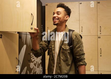 Young attractive African American man happily opening locker in office cloakroom Stock Photo