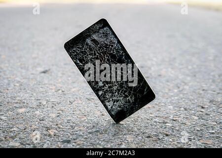 Phone while falling on the road. Mobile phone cracks on impact on concrete. Modern smartphone with highly broken screen dropped on the asphalt. Stock Photo
