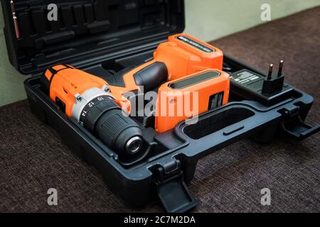 Cordless orange drill with black battery. orange screwdriver or drill in a black container lies on the floor. Tool for tightening screws. screw gun Stock Photo