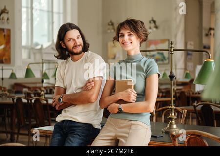 Young attractive smiling students with notepad happily looking in camera in library of university Stock Photo