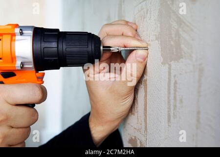 Screwing a screw into wall with an electric screwdriver close-up. Repair in the apartment or house. Stock Photo