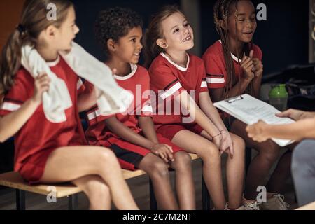 Kids sport team in changing room.Young players sitting on bench. Stock Photo