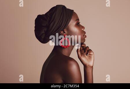 Side view of a woman wearing black turban against beige background. African female model with beautiful skin posing in studio.